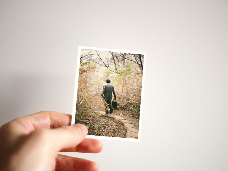 a man in suit with briefcase walking away on a trail in a forest